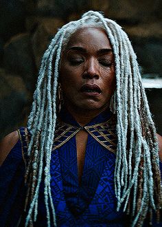 a woman with white dreadlocks standing in front of a stone wall