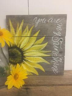 two yellow sunflowers sitting on top of a wooden table next to a vase