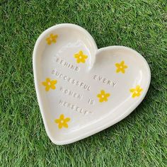 a ceramic heart shaped dish with yellow flowers on it sitting in the grass, saying beware every successful women is here