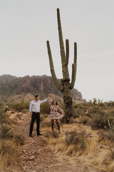 a man and woman dancing in front of a large saguado cactus with mountains in the background