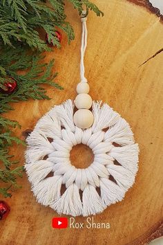 an ornament made out of yarn and beads sits on a wooden board next to christmas tree branches