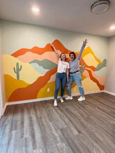 two people standing in an empty room with mountains painted on the wall and wood floors