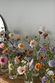 several vases filled with different colored flowers on a wooden table next to a mirror