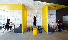 two women are sitting at tables in an office with yellow and black accents on the walls