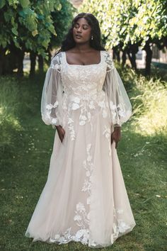 a woman in a wedding dress standing on the grass with trees behind her, wearing an off - white gown