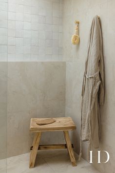 a wooden bench sitting next to a white tiled shower stall with a coat hanging on the wall