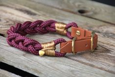 a purple and gold rope bracelet with brass clasps on a wooden bench, close up