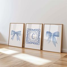 three framed pictures with blue bows are on the floor in front of a white wall