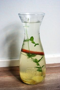 a glass vase filled with water and green leaves on top of a wooden floor next to a wall