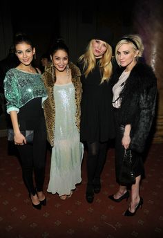 three women standing next to each other in front of a dark room with red carpet