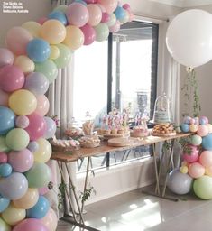 an arch made out of balloons in the middle of a room with a table full of desserts