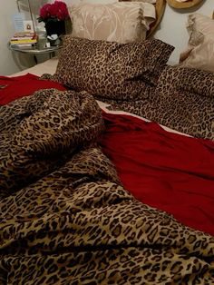 a leopard print comforter on a bed with red sheets and pillows, in front of a round mirror