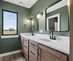 a bathroom with green walls and white counter tops next to a large window in the corner