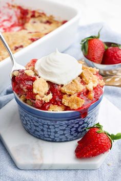 strawberry cobbler with whipped cream on top in blue bowl next to fresh strawberries