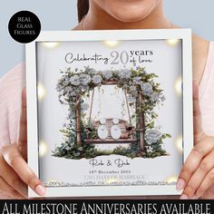 a woman holding up a photo frame with flowers and lights on it that reads celebrating 20 years of love