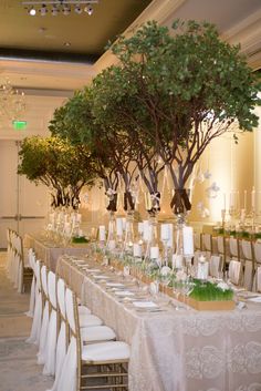 a long table is set with white linens and green centerpieces