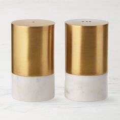 two gold and white ceramic salt and pepper shakers on a marble countertop, one with a golden top