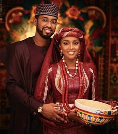 a man and woman dressed in traditional african garb holding a bowl with beads on it