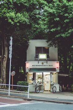 a small building sitting on the side of a road next to a street sign and trees