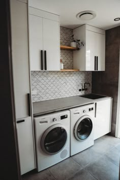 a washer and dryer in a small room with white cupboards on the wall