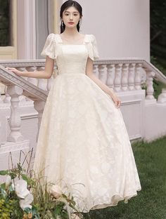 a woman in a white dress is standing on the grass near some stairs and flowers