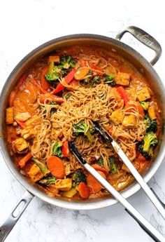 a pan filled with noodles and vegetables on top of a white counter next to utensils