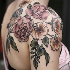 the back of a woman's shoulder with flowers and leaves tattooed on her arm