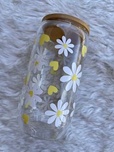 a clear glass with yellow and white flowers painted on the side is sitting on a furry surface