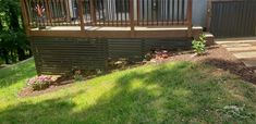 a wooden deck in the middle of a yard with grass and flowers on the ground