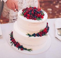 a man and woman cutting into a white cake with berries on it at a wedding reception