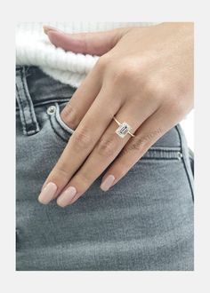 a woman's hand with a diamond ring on her left finger, wearing grey jeans