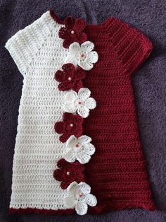 a red and white crocheted dress with flowers on the side, sitting on a purple blanket