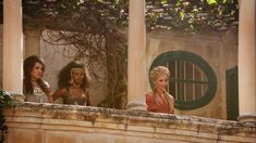 three women standing on the balcony of an old building with columns and ivy growing around them