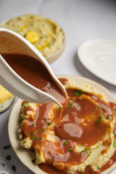 a person pouring sauce over mashed potatoes on a plate