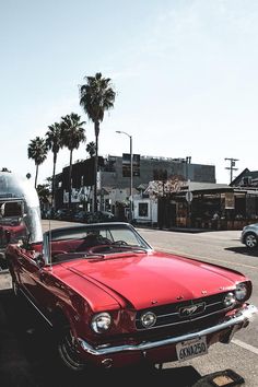 an old red car is parked on the side of the road with palm trees in the background