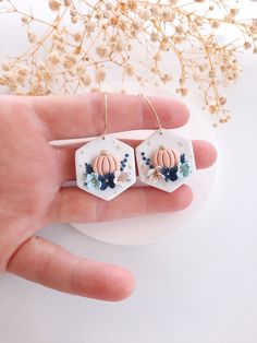 a hand holding two small ceramic pumpkins on top of it's ear wires