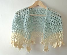 a crocheted shawl is hanging on a wooden hanger with a white wall in the background