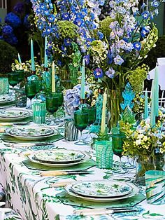 the table is set with green glassware and blue flowers