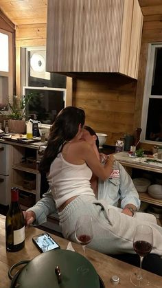 a man and woman sitting in a kitchen next to each other with wine glasses on the table