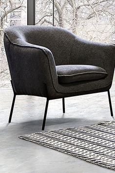 a gray chair sitting on top of a rug in front of a large window with trees outside