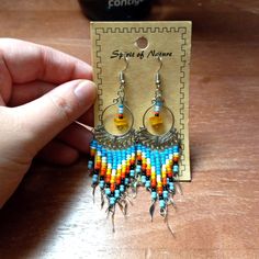 a pair of colorful beaded earrings is being held by a person's hand