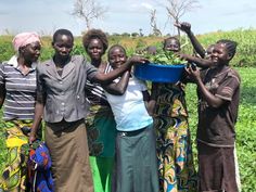 a group of women standing next to each other in front of a field with crops