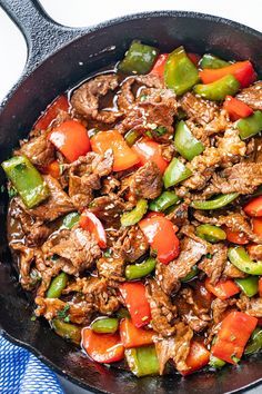 a skillet filled with beef and peppers on top of a blue checkered table cloth