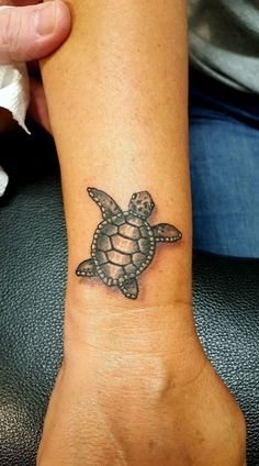 a small turtle tattoo on the wrist is shown in black and grey ink, with an intricate design