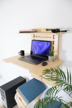 an open laptop computer sitting on top of a wooden desk next to a potted plant