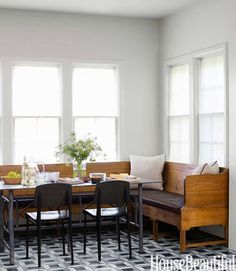 a dining table with four chairs and a bench in front of two large windows on the wall