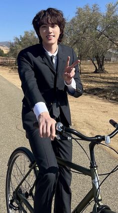 a man in a suit is riding a bike on the side of the road with his hand up