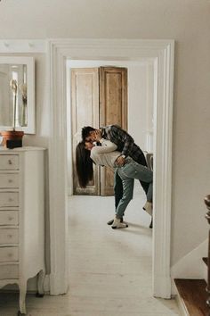 a man and woman are kissing in the hallway between two white dressers on either side of each other