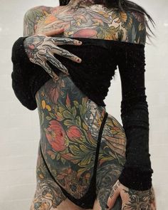 a woman with tattoos on her body posing for the camera and holding her hands behind her back