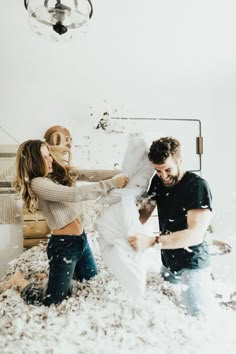 two people are throwing pillows in the air while another person is standing on top of them